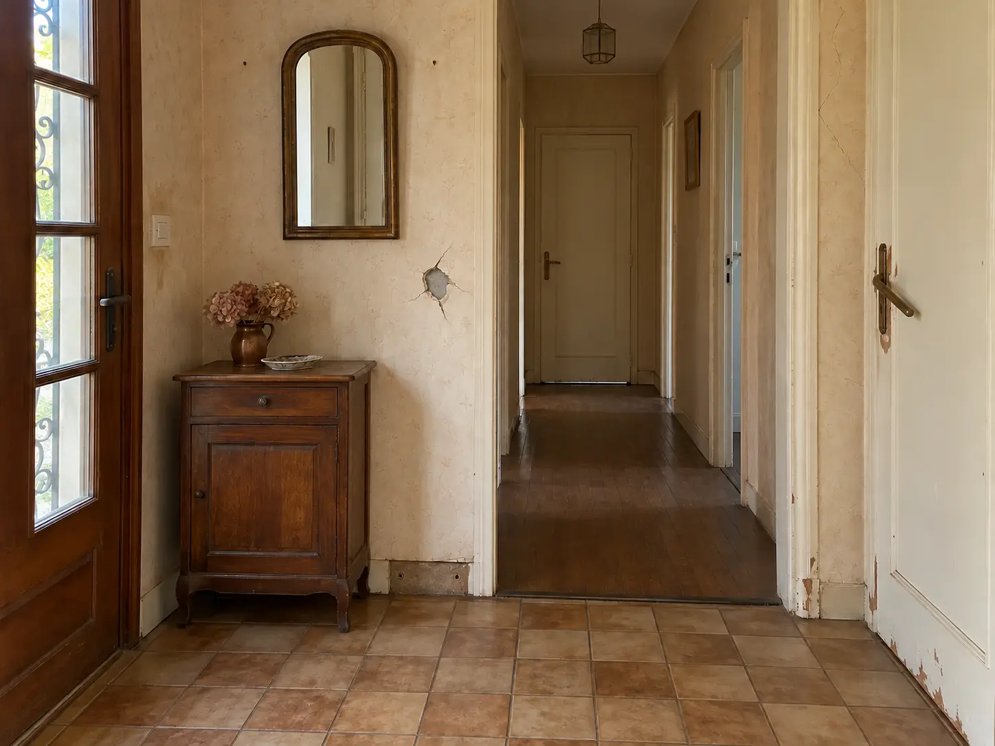 Entrée ancienne avant intervention, avec un trou dans le mur, une plinthe manquante et une poignée abîmée